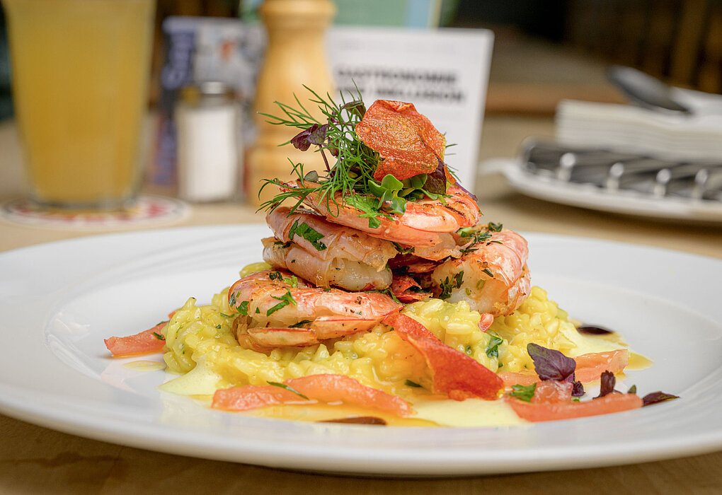 Ein Teller mit cremigem Risotto, darauf mehrere gebratene Garnelen, garniert mit frischen Kräutern und roten Chips.